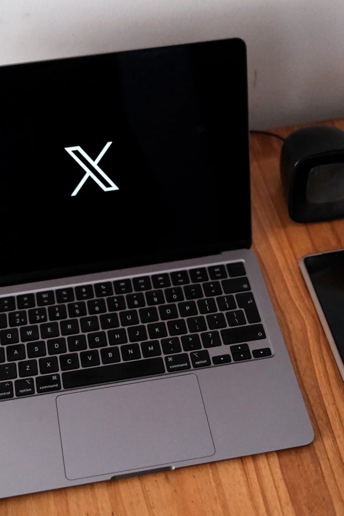 Minimalist desk setup featuring a laptop, smartphone, and clock on a wooden surface.